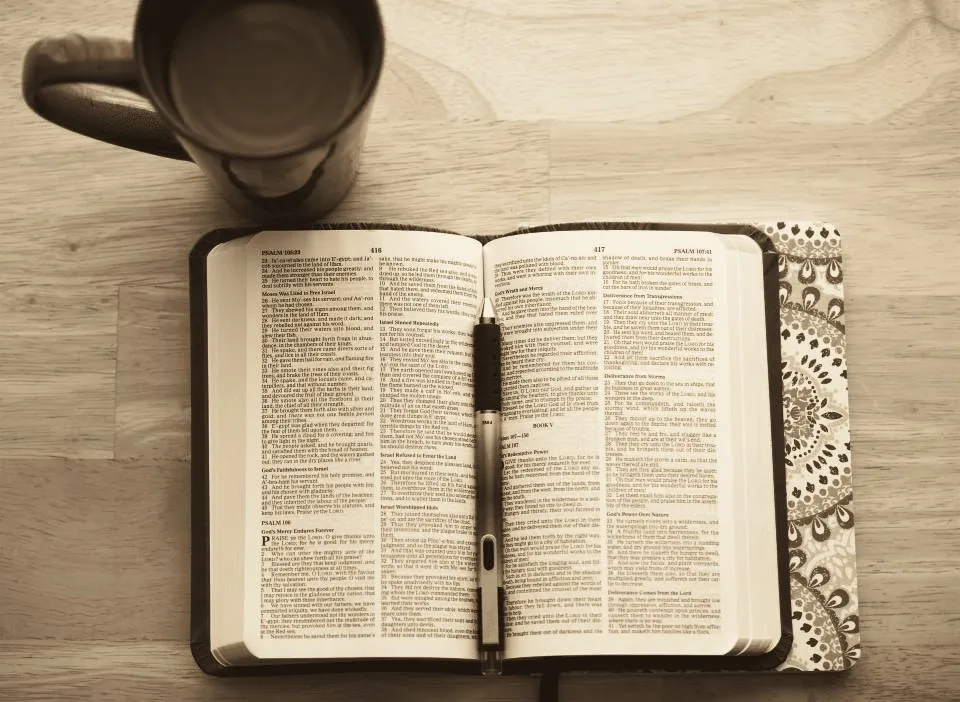 An open Bible and a mug of coffee on a wooden table